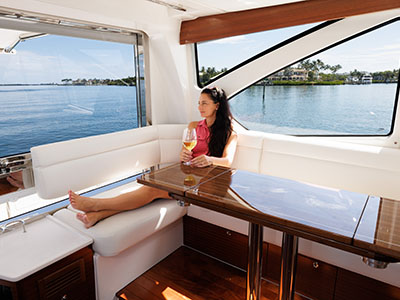 A woman seated at the salon dinette of a Pursuit OS 445 with a glass of wine and a water view.