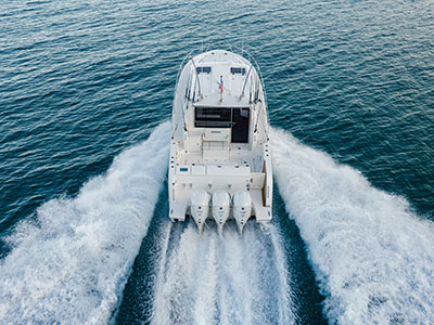 Stern view of a Pursuit OS 445 running away from the camera on quad outboards.
