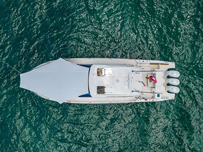 Overhead view of a Pursuit OS 445 at anchor with the bow sunshade deployed over green water.