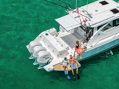 Two people in snorkel fins seated on the swim platform of a Pursuit OS 445 over green water.