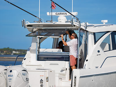 A man at the aft station of a Pursuit OS 445 under the hardtop, Garmin electronics overhead.