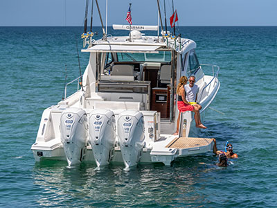 Stern quarter view of a Pursuit OS 445 at rest showing quad Yamaha 450 outboards, with a snorkeler alongside.