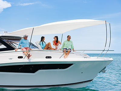 Group seated on the bow of a Pursuit OS 445 with the sunshade deployed over turquoise water.