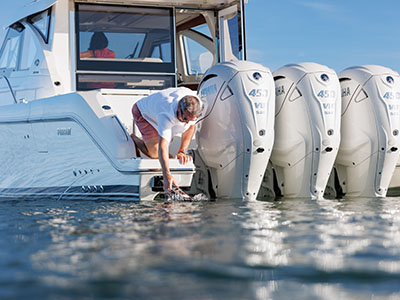 A man reaching into the water at the transom of a Pursuit OS 445 beside the Yamaha 450 outboards.