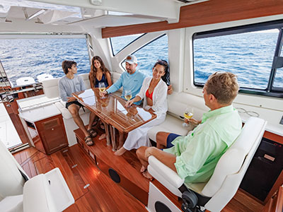 Group seated around the salon dinette of a Pursuit OS 445 with teak joinery and helm seats forward.