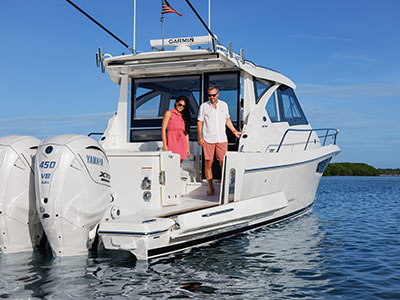 Two people standing in the cockpit doorway of a Pursuit OS 445, seen from astern.