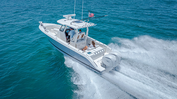 Pursuit center console boat running on open water with a man at the helm, a child seated beside him, and a woman relaxing on the rear bench seat.