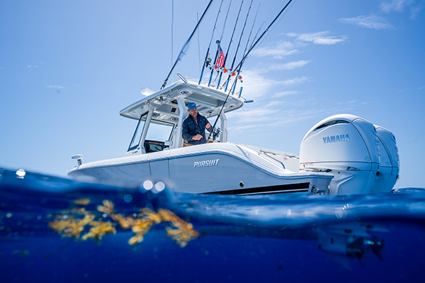 Split-level photo of a Pursuit boat showing a man fishing from the deck above the waterline and floating sargassum seaweed below it.