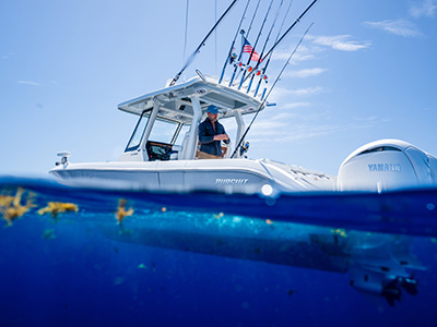 Split-level photo of a Pursuit boat with a man standing on deck above the waterline and drifting sargassum seaweed visible underwater below.