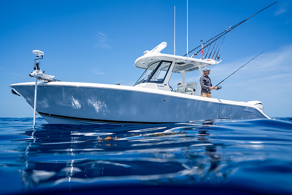 Pursuit S 288 center console boat viewed from water level, with a man fishing from the deck and another seated near the helm.