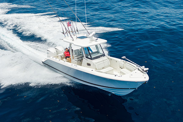 Pursuit S 288 center console boat running at speed on open water, viewed from above, with two people seated in the cockpit and multiple fishing rods mounted on the hardtop.