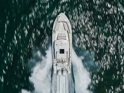 Aerial overhead view of a Pursuit center console boat running away from the camera through green water, showing the open cockpit deck and a twin-engine wake fanning out behind it.