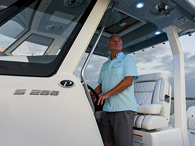 Man standing at the helm of a Pursuit S 288 center console boat at dusk, with the model badge visible on the console beside him.