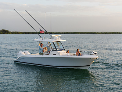 Pursuit center console boat anchored near a mangrove shoreline at dusk, with four people aboard, two of them seated with drinks.