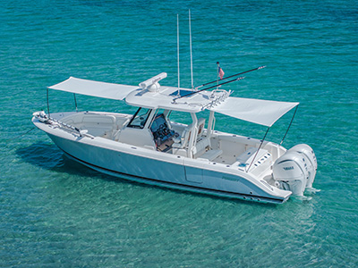 Pursuit center console boat anchored in clear turquoise water, viewed from the side with its sun shade extended and no one visible on deck.