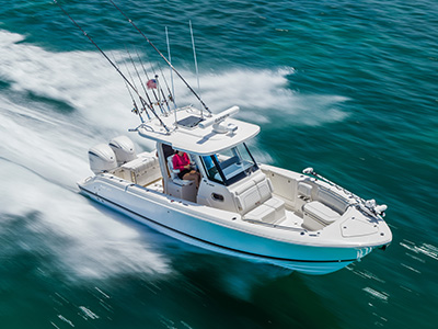 Aerial view of a Pursuit center console boat with a light blue hull running at speed, showing a woman seated near the helm and rod holders lined across the hardtop.