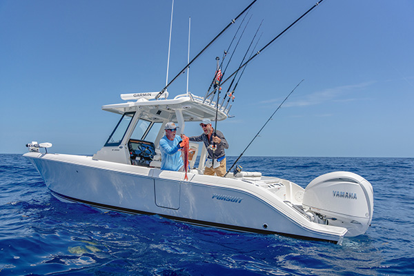 Two men on a Pursuit boat holding up a freshly caught red snapper, with a Yamaha outboard engine visible at the stern.