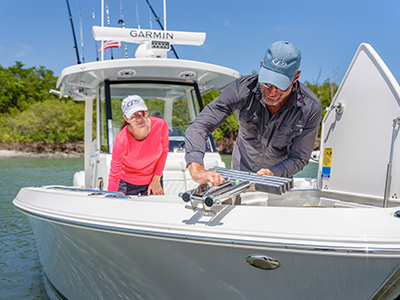 Man and woman working together to install a rod holder rack into an open deck hatch on a Pursuit boat, with a mangrove shoreline in the background.