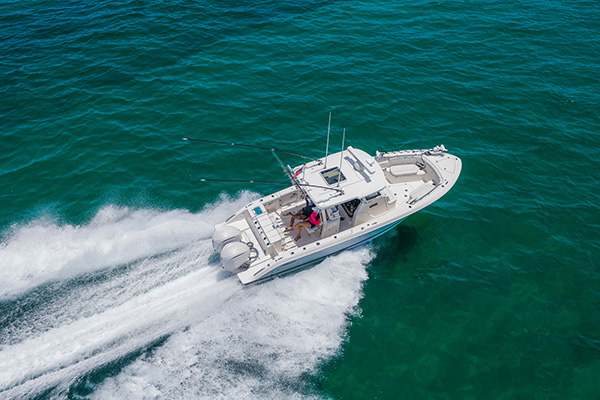 Pursuit center console boat turning on turquoise water, with two people seated together in the cockpit and twin outboard engines producing a white wake.