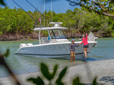 Pursuit boat beached bow-first near a mangrove shoreline, with a man and woman stepping off the bow onto the sand.