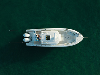 Aerial overhead view of a Pursuit center console boat on dark green water with two fishing rods extended horizontally from the sides and two people standing near the console.