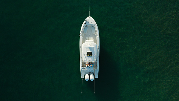 Aerial overhead view of a Pursuit center console boat on dark green water with two people seated near the stern and fenders hanging off the back.