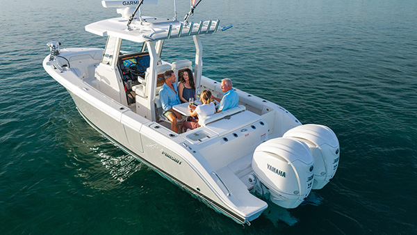 Pursuit center console boat anchored on calm water with four people seated together around a small table sharing drinks in the cockpit.