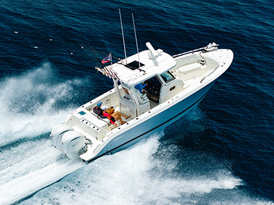 Aerial view of a Pursuit center console boat running at speed on dark blue water, with two women seated together in the cockpit and a man at the helm.