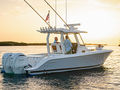 Pursuit center console boat idling at sunset with two men standing near the helm and a woman seated at the stern, sailboats visible in the distance.