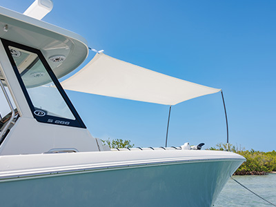Close-up of the bow of a Pursuit S 288 center console boat with a shade canopy extended, a mangrove shoreline visible in the background.