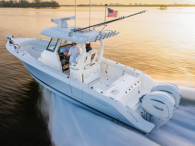 Aerial view of a Pursuit S 288 center console boat running at sunset with two people at the helm and dual Yamaha outboard engines visible at the stern.