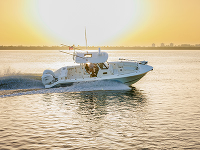 Pursuit center console boat running at sunset, backlit by the sun with two people seated near the helm silhouetted against the glowing water.