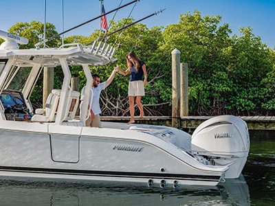 Man on a Pursuit boat holding hands with a woman as she steps onto a wooden dock lined with mangroves.