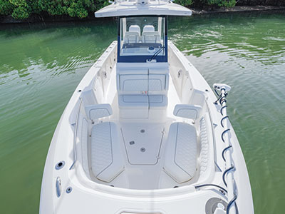 Aerial view looking down the bow of a Pursuit center console boat anchored near a mangrove shoreline, showing empty white quilted seating and a Garmin trolling motor mounted at the bow.
