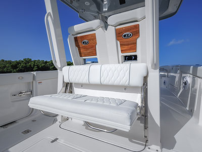 Close-up of a folded helm seat backrest and bench on a Pursuit boat, showing wood-accented Pursuit logo panels and a speaker grille, with another boat visible in the background.