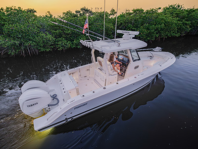Pursuit center console boat running through a mangrove-lined channel at dusk, with a woman seated near the helm operating the display and a man at the wheel.