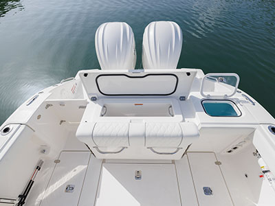Overhead view of a Pursuit boat's open transom compartment showing an empty livewell, twin outboard engines, and a folded bench seat with storage hatches on either side.