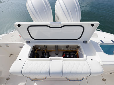 Close-up overhead view of an open transom hatch on a Pursuit boat revealing battery banks and wiring, with twin outboard engines and a livewell visible nearby.