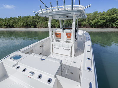 View from the bow toward the helm of a Pursuit boat anchored near a mangrove shoreline, showing rocket launcher rod holders on the hardtop and a folded bench seat with cup holders.