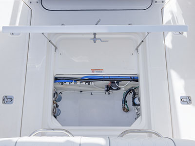 Overhead view looking down into an open bulkhead compartment on a Pursuit boat, showing plumbing lines and pumps beneath a warning label about not drilling into the bulkhead.