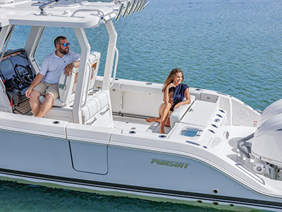 A man seated at the helm and a woman seated on a bench seat near the stern of a Pursuit boat, both smiling, with a Yamaha outboard engine visible at the transom.