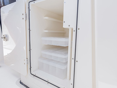 Close-up of an open tackle storage compartment on a Pursuit boat, showing three pull-out plastic tackle trays on sliding shelves.