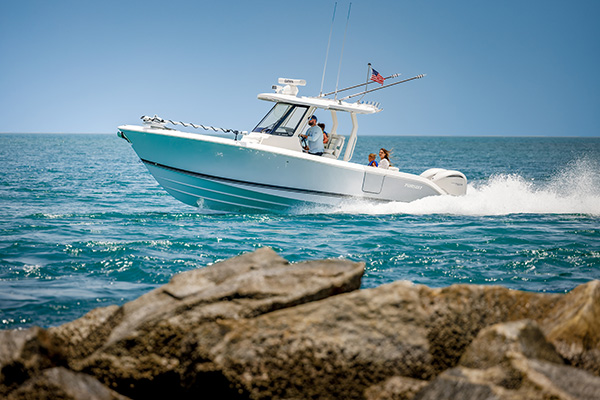Pursuit center console boat running past a rocky shoreline, with a man and two children near the helm and a woman standing at the stern.