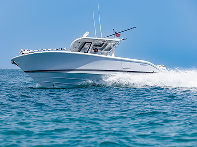 Pursuit center console boat running at speed with a man at the helm, viewed from the water with the boat's wake spraying behind it.