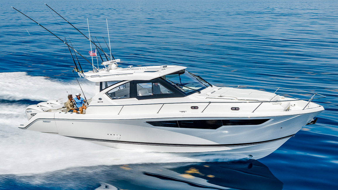 Pursuit OS 445 underway on calm blue water with a person standing at the bow rail.