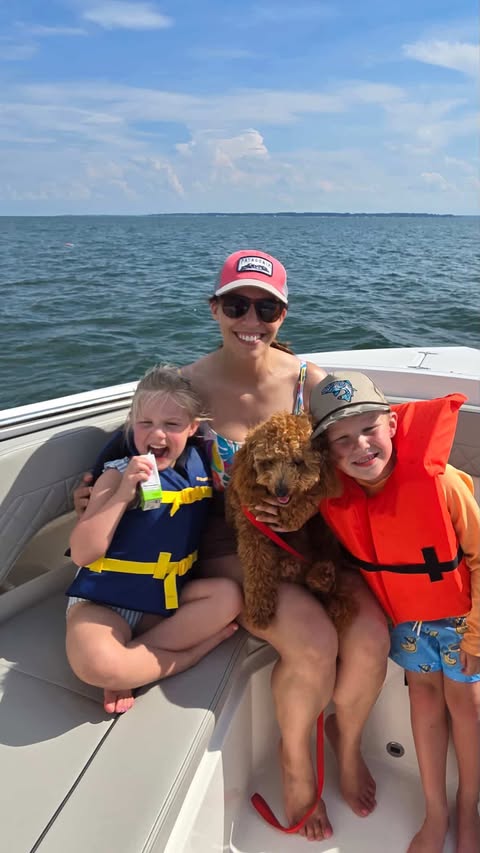 A woman with two children and a dog sits on the bow of a boat and smiles.